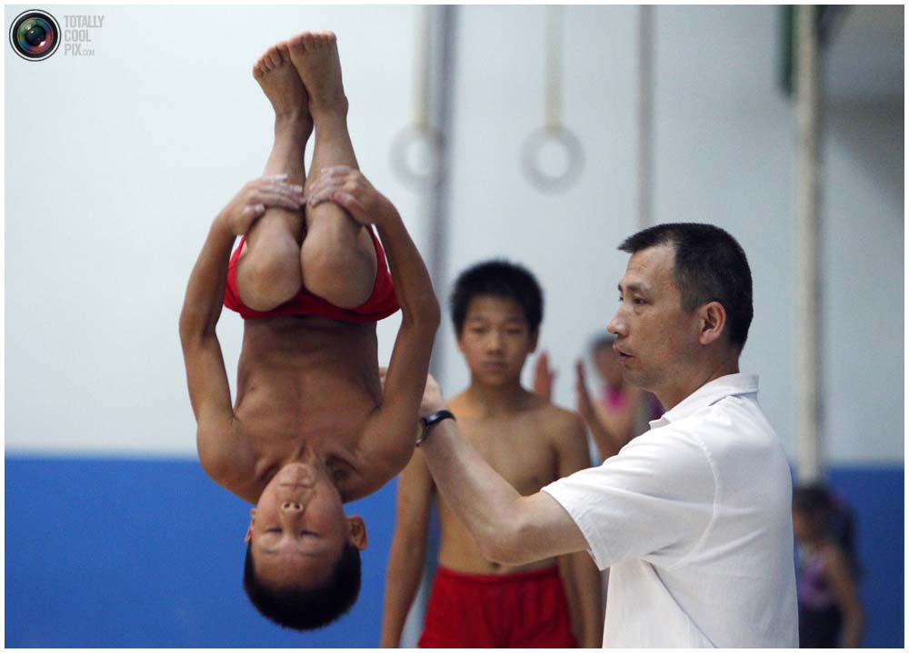 Тренер помогает мальчику в спортивной школе Шичахай в Пекине, 18 августа 2010 года. (REUTERS/David Gray)