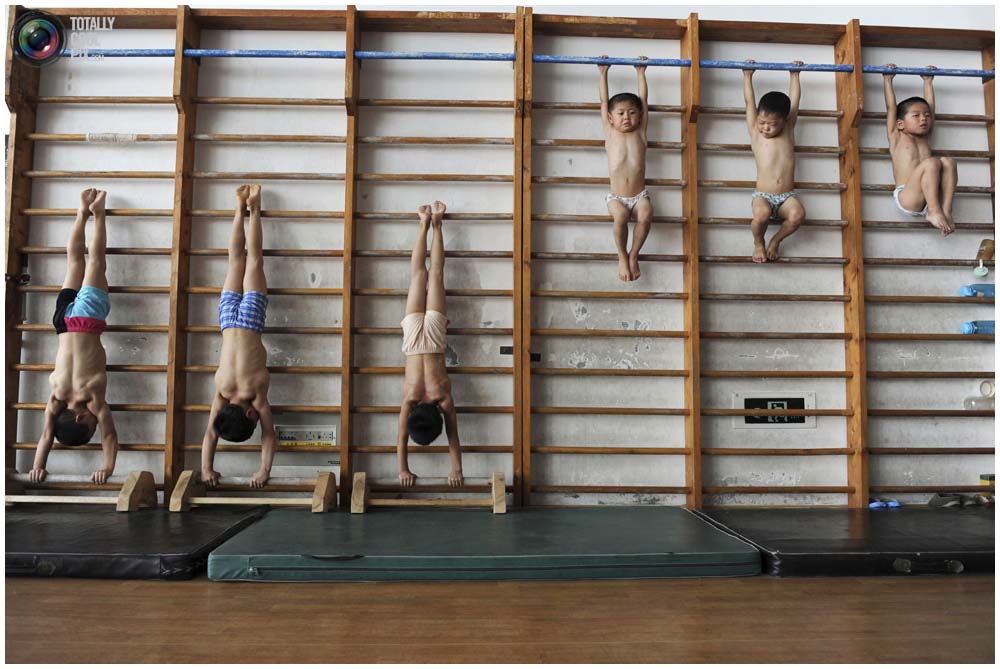 Маленькие гимнасты из группы 4-7 лет растягиваются на шведской стенке в гимнастическом зале в городе Цзясин, провинция Чжэцзян, 10 августа 2010 года. (REUTERS/Stringer) 